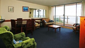A spacious living room with a large window, a dining table, and two sofas. - Ebbtide Unit 33 (Forster)