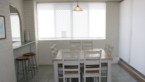 En matplats med ett vitt bord och stolar, ett fönster med utsikt och en bardisk med barstolar.