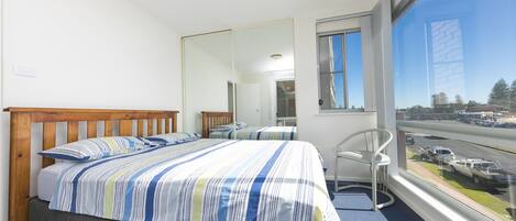 A hotel room with a bed, a chair, a large window, and a view of the street.