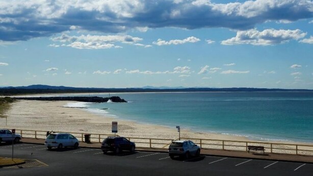A parking lot with cars parked near a beach, a clear sky, and a distant view of the ocean. - El Sandi Unit 10 (Forster)