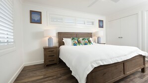 Une chambre à coucher avec un lit en bois, une literie blanche, une table de chevet avec une lampe et un ventilateur de plafond.