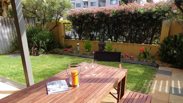 A wooden patio table with a magazine, a candle, and two wine glasses. - Gwydir Court 1 (Forster)