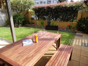 A wooden patio table with a magazine, a candle, and two wine glasses. - Gwydir Court 1 (Forster)