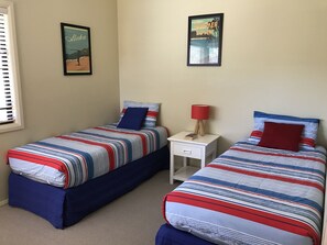 A bedroom with two beds, each with striped bedding and pillows, a nightstand with a lamp, and framed pictures on the wall.