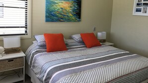 A bedroom with a bed, two pillows, a nightstand, a lamp, a painting, and a window with blinds. - Gwydir Court 1 (Forster)