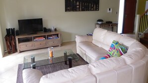 A living room with a beige sofa, a glass coffee table, a TV on a wooden stand, and a painting on the wall. - Gwydir Court 1 (Forster)