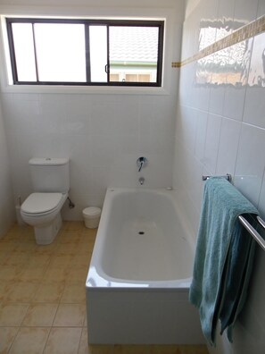 A bathroom with a bathtub, toilet, and window.