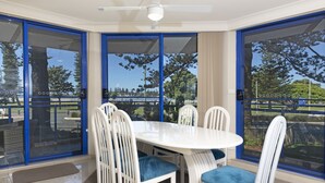 A dining area with a white table and chairs, large glass doors, and a ceiling fan. - Heritage 101 (Tuncurry)