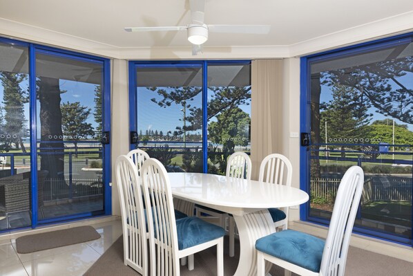 A dining area with a white table and chairs, large glass doors, and a ceiling fan. - Heritage 101 (Tuncurry)
