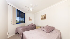 A room with two beds, a ceiling fan, a window with a view, and a small table. - Heritage 101 (Tuncurry)