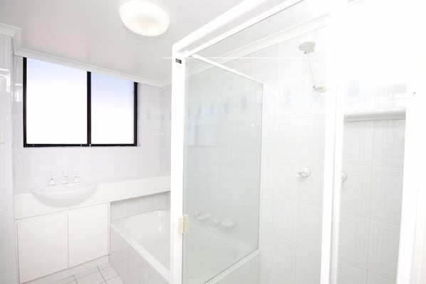 A modern bathroom with a white sink, bathtub, and glass-enclosed shower.
