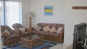 A living room with wicker furniture, a glass coffee table, a television, and a colorful rug. - Hi Surf Unit 2 (Forster)