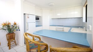 A modern kitchen with white cabinets, a blue countertop, and wicker chairs. - Hi Surf Unit 2 (Forster)