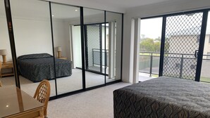 A hotel room with a bed, a table, a chair, a large mirror, and a balcony with a view. - Hi Surf Unit 4 (Forster)