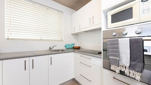 A modern kitchen with white cabinets, a microwave, an oven, and a sink. - Hibiscus Court Unit 4 (Forster)
