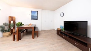 A living room with a wooden dining table, a flat-screen TV on a wooden stand, a white wardrobe, and a small potted plant. - Hibiscus Court Unit 4 (Forster)