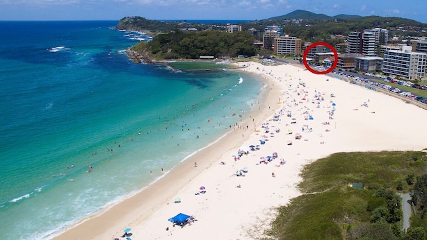 A beach with a clear view of the ocean, a sandy shore, and a building complex in the background. - Hibiscus Court Unit 4 (Forster)