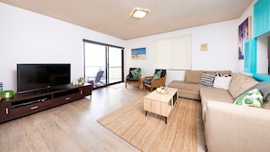 A modern living room with a flat-screen TV, a sofa, a coffee table, and a wicker chair. - Hibiscus Court Unit 4 (Forster)