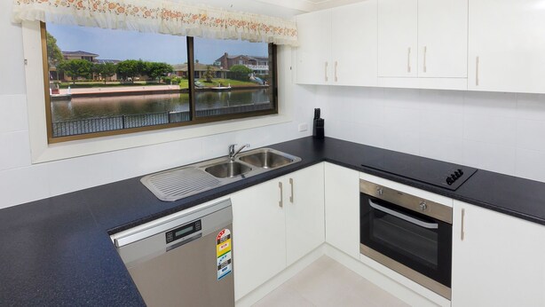 A kitchen with white cabinets, a black countertop, a dishwasher, and an oven. - Lake House on Elouera (Forster)