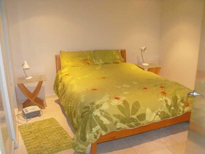 A bedroom with a bed, a nightstand, a lamp, and a small table with a power strip.