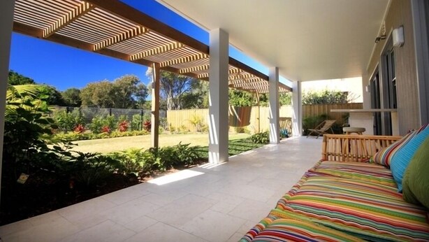 Un patio cubierto con una cama, una maceta colgante y vistas a un jardín.