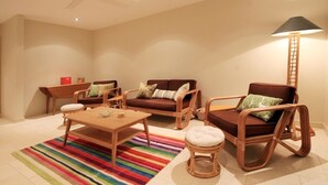 Una sala de estar con una mesa de centro de madera, dos sofás marrones con cojines, un tapete a rayas, una lámpara de pie y un ventilador de techo.