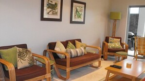 Una sala de estar con un sofá, dos sillones, una mesa de centro y una lámpara. Hay dos cuadros enmarcados en la pared.