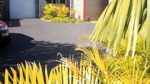 Una casa moderna de dos pisos con garaje, rodeada de jardines cuidados y palmeras.