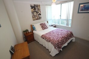 A bedroom with a bed, a nightstand, a wooden bench, a wall art piece, and a window with blinds. - Mirage Unit 101 (Tuncurry)