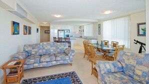 A spacious living room with a large sofa set, a dining table with chairs, and a kitchen area in the background. - Mirage Unit 602 (Tuncurry)
