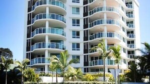 A multi-story hotel with a curved facade, balconies on each floor, and a landscaped front yard with palm trees. - Mirage Unit 602 (Tuncurry)