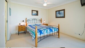 A bedroom with a bed, bedside tables, a ceiling fan, and two framed pictures on the walls. - Mirage Unit 602 (Tuncurry)