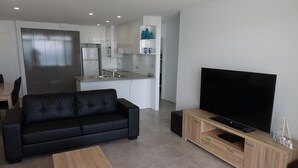 Ein modernes Wohnzimmer mit einem schwarzen Ledersofa, einem Holztisch und einem Fernseher auf einem Holzständer.