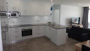 Eine moderne Küche mit weißen Schränken, einer Mikrowelle, einem Backofen und einem Geschirrspüler. Es gibt eine Essecke mit Tisch und Stühlen und im Eck steht ein Fernseher.