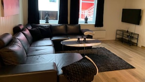A modern living room with a leather sofa, a small coffee table, and a TV on the wall. - Notodden Sentrum Apartment No 1 (Notodden)