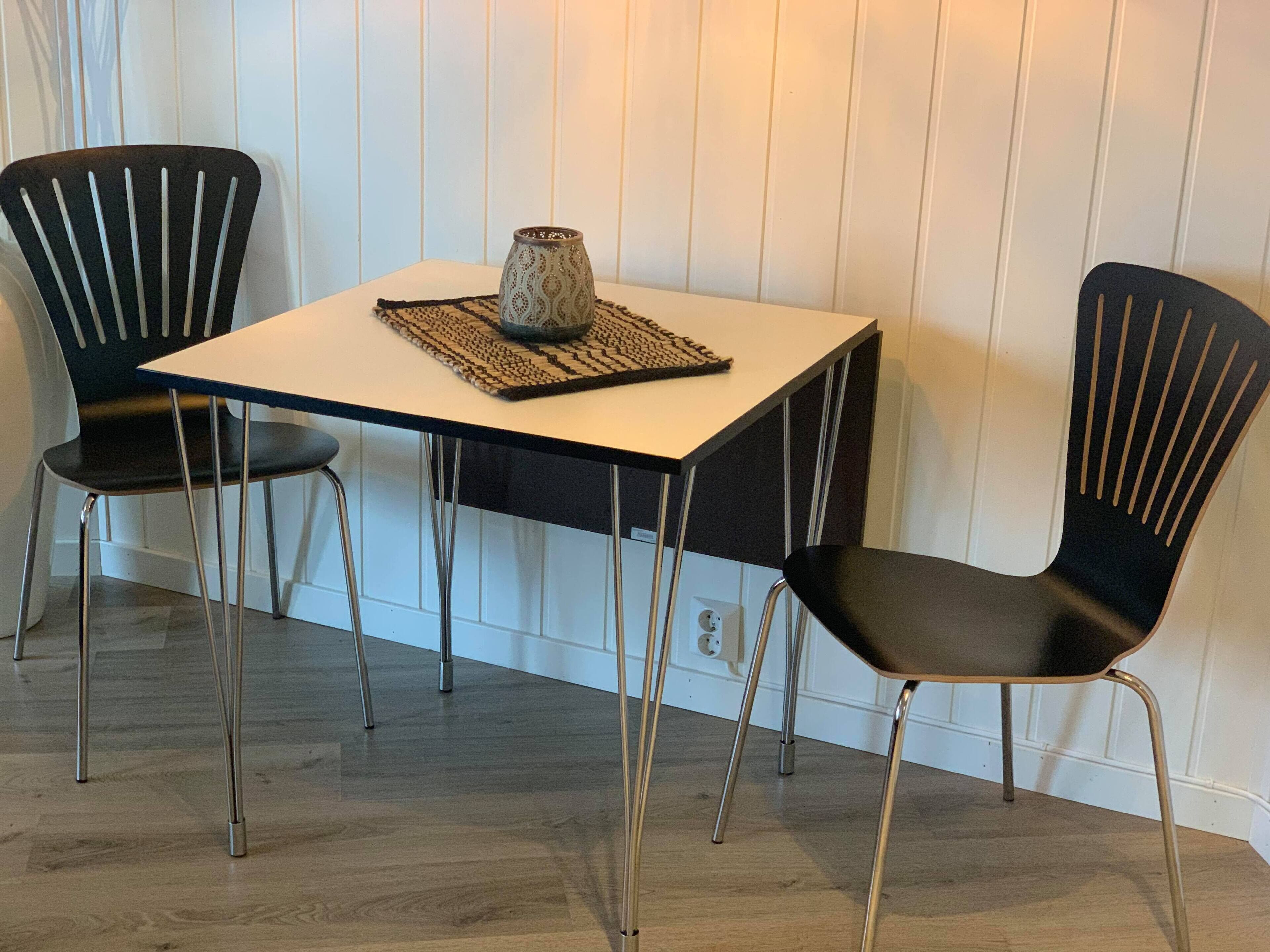 A small dining area with a white table and two black chairs with gold legs.