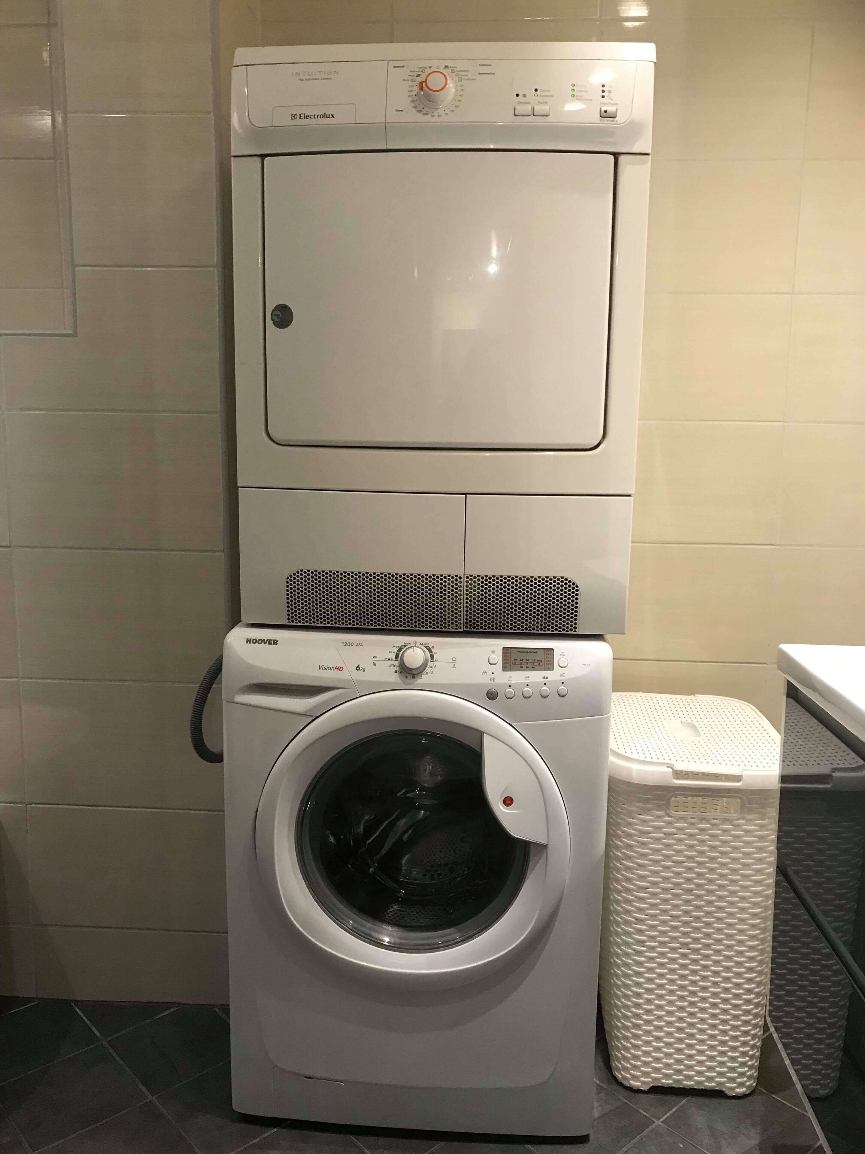 A front-loading washer and dryer unit with a control panel, a hose, and a plastic laundry basket.