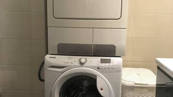 Lavadora y secadora apilables con panel de control, una manguera y una cesta de plástico para ropa.