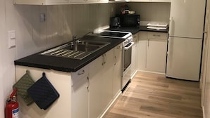 A compact kitchen with white cabinets, a black countertop, a stove, a microwave, and a refrigerator. - Notodden Sentrum Apartment No 1 (Notodden)