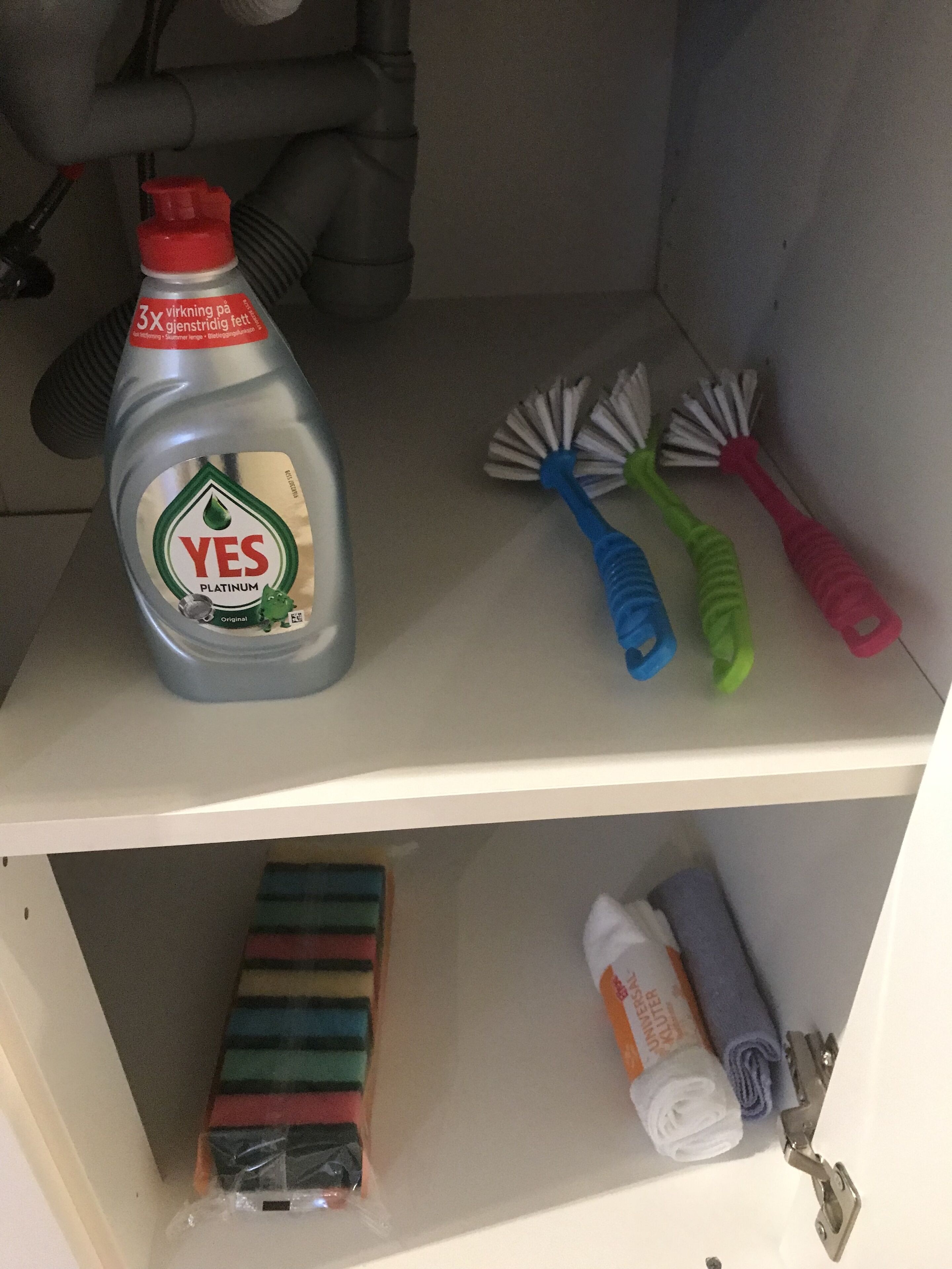 Uno scaffale con una bottiglia di detergente YES Platinum, una spazzola blu e verde e una spazzola rosa.