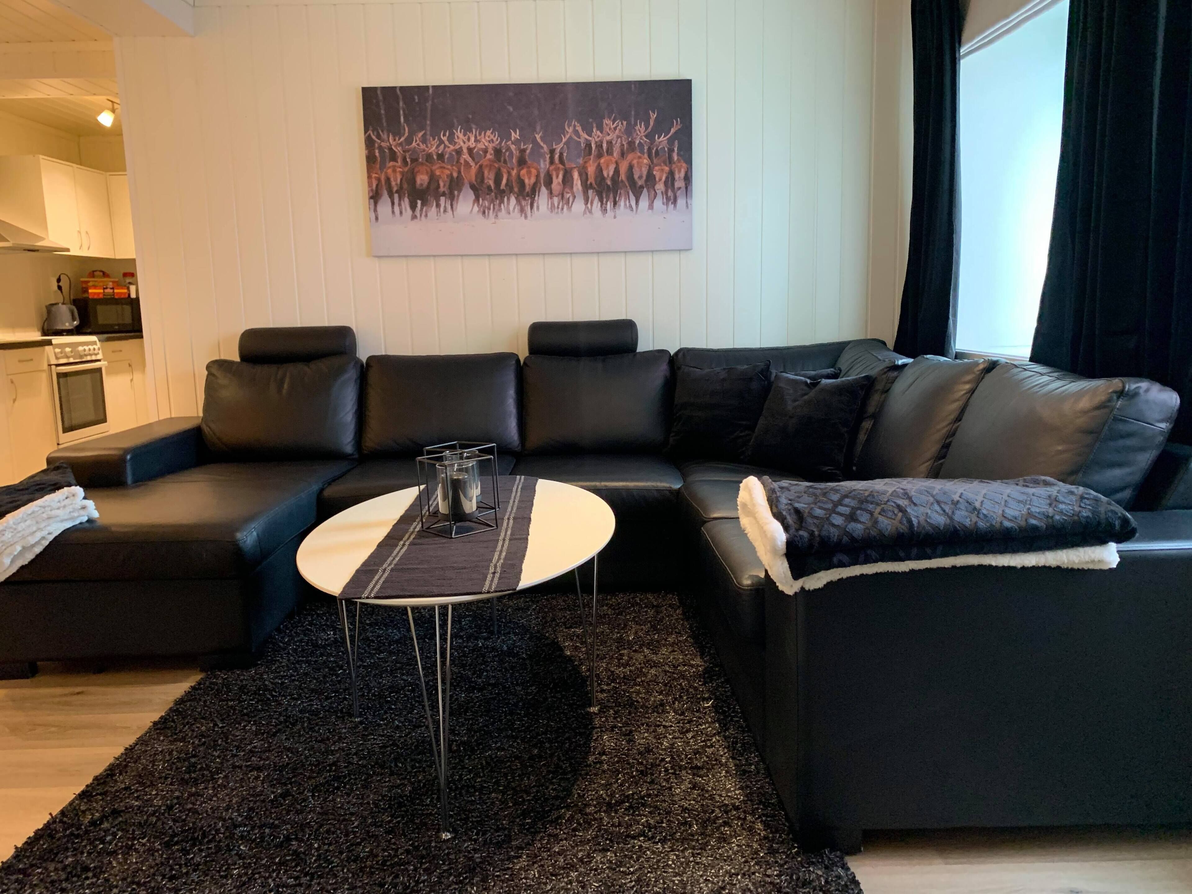Uma sala de estar moderna com um sofá de couro preto, uma mesa de centro redonda e uma pintura de veados na parede.