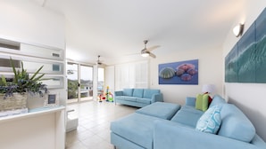 A spacious living room with a light blue sofa, a ceiling fan, and a view through a glass door to the outside. - One Mile House (Forster)