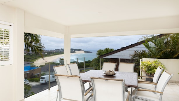 A balcony with a table and chairs, overlooking a beach and a residential area. - One Mile House (Forster)