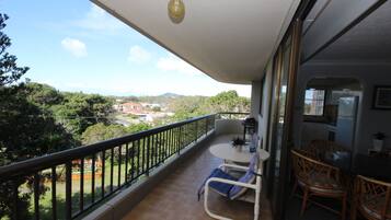A balcony with a view of a residential area, a small table with chairs, and a potted plant.