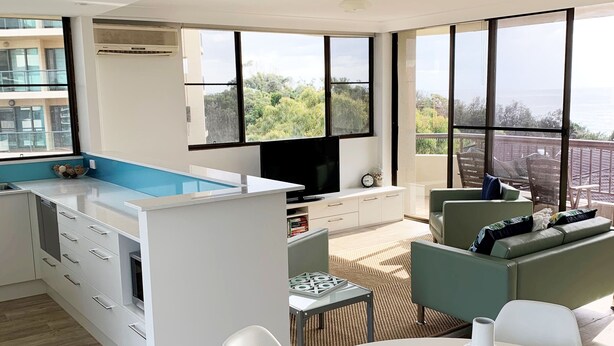 A modern kitchen with a large island, a dining area with a round table, and a living area with a sofa and chairs. - Pinnacle Unit 701 (Forster)