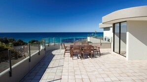 A rooftop terrace with a view of the ocean, a table with chairs, and a glass railing. - Pinnacle Unit 701 (Forster)