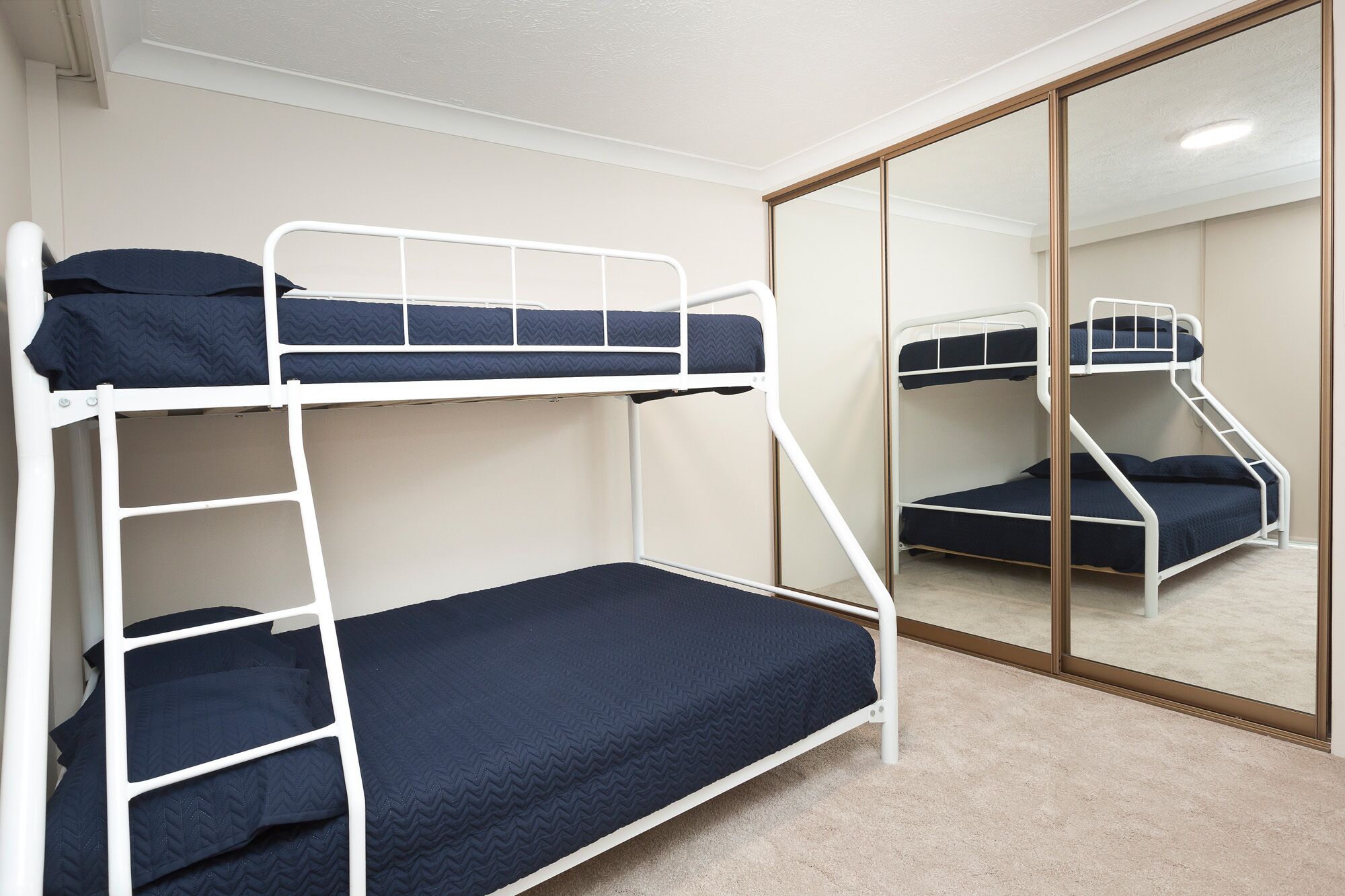 A bunk bed room with a mirror and a carpeted floor.