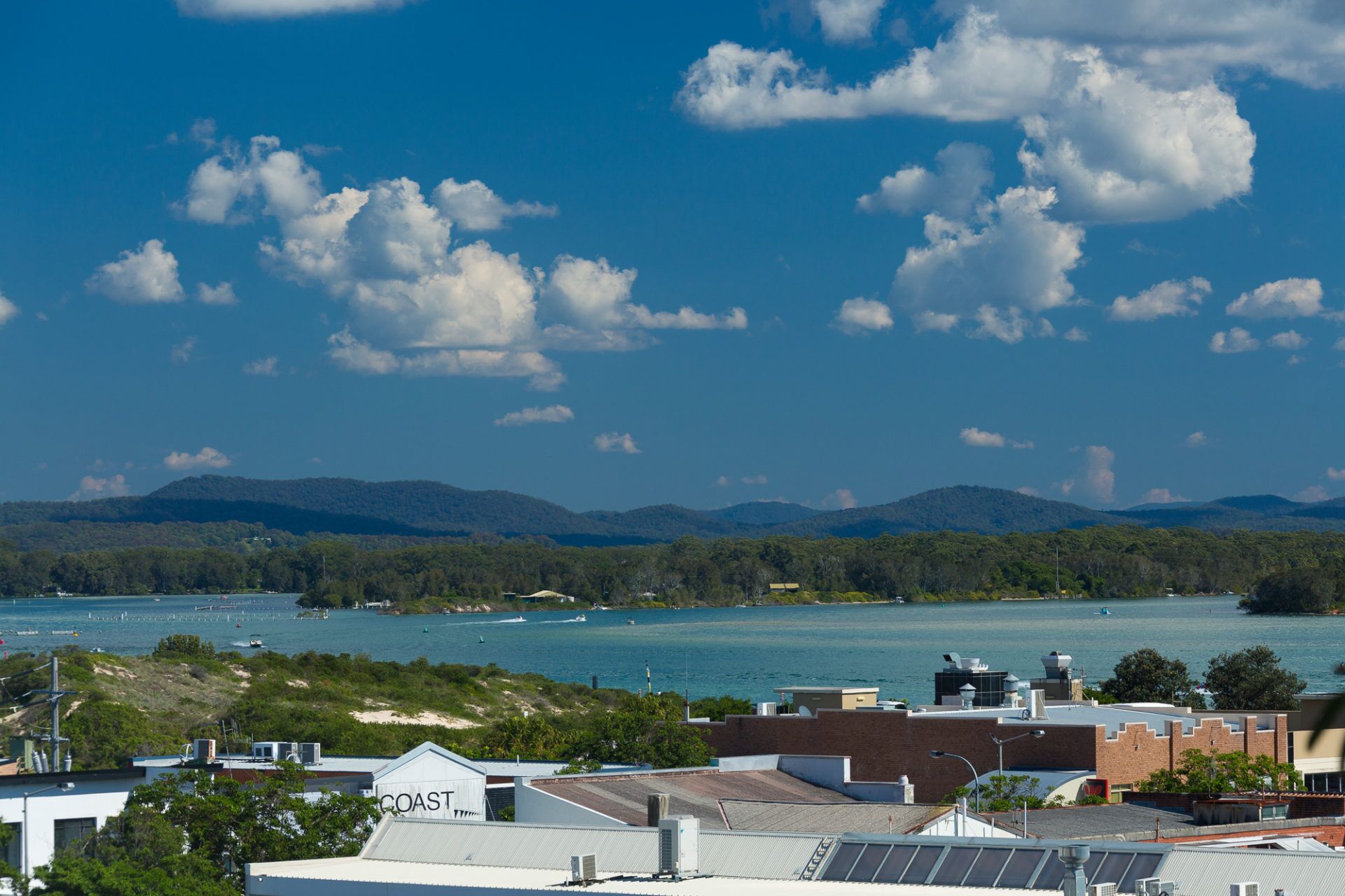 A coastal view with buildings, a marina, and mountains in the background.
