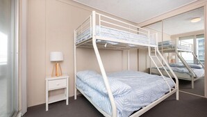 Ein Schlafraum mit Etagenbetten, einem kleinen Nachttisch und Lampe, einem Spiegel an der Wand und einem Fenster.