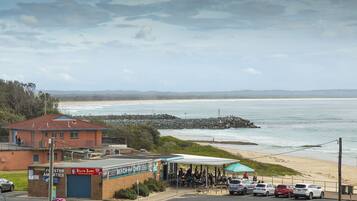 A beachside cafe with outdoor seating, a parking area, and a view of the ocean.